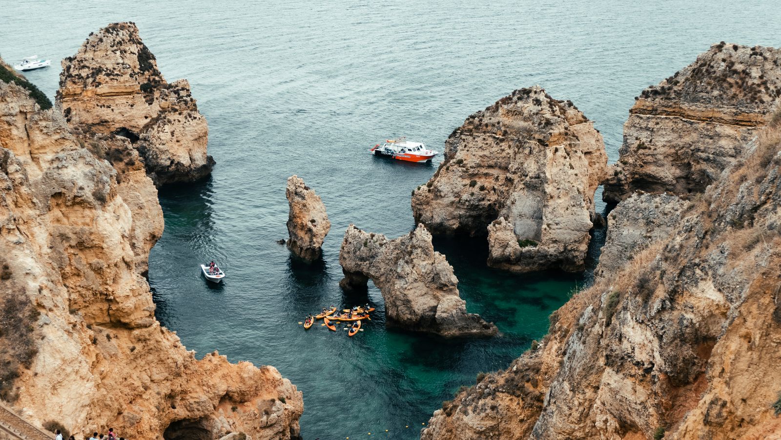 Boats in turquoise water below sea cliffs, seen from above