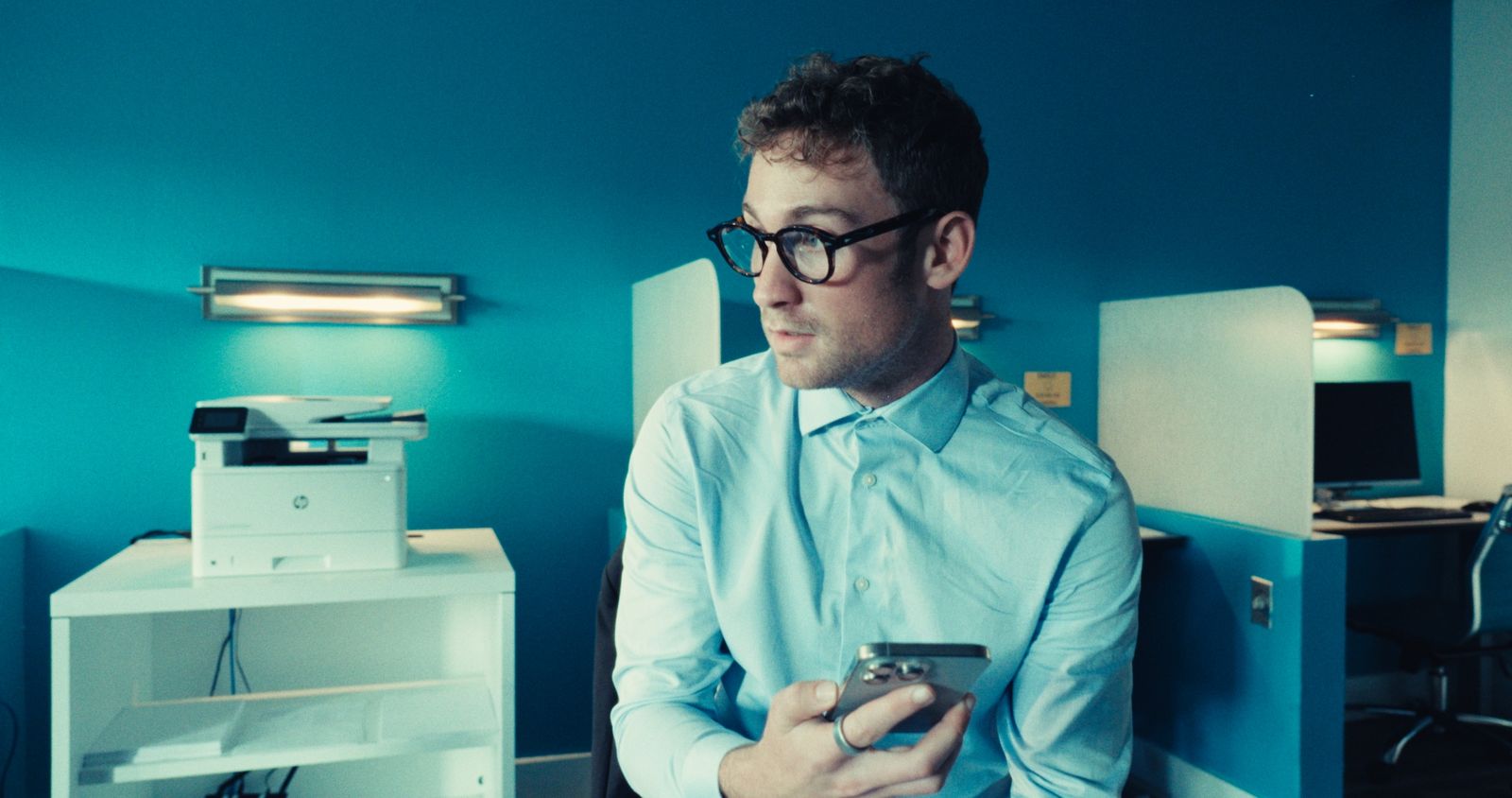 A man in glasses in a blue-lit office