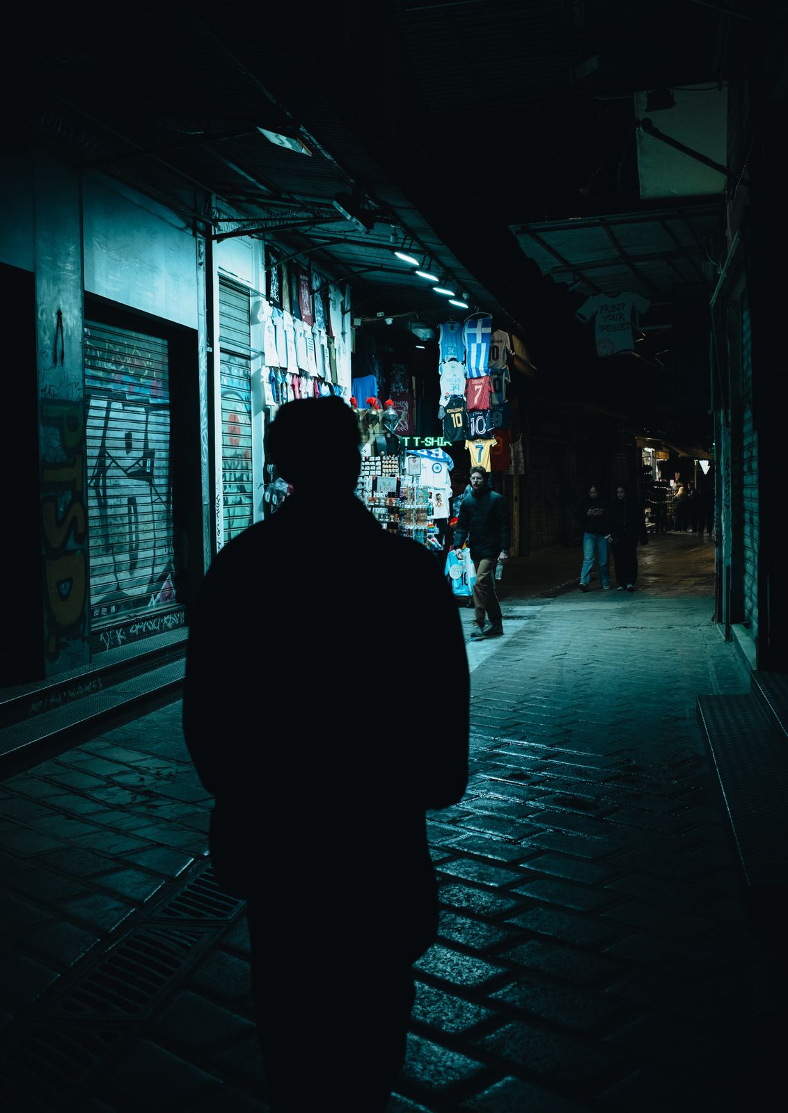 A figure walking through a dark, neon-lit alley
